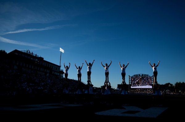 Cheerleaders are silhouetted in formation against a blue sky in a football stadium. 