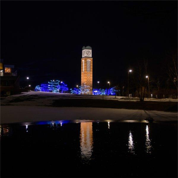 Cook Carillon tower at night with blue lights in trees that are reflected on pond in front