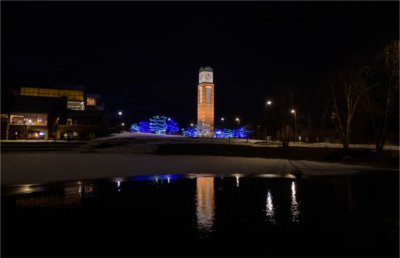 Cook Carillon tower at night with blue lights in trees that are reflected on pond in front