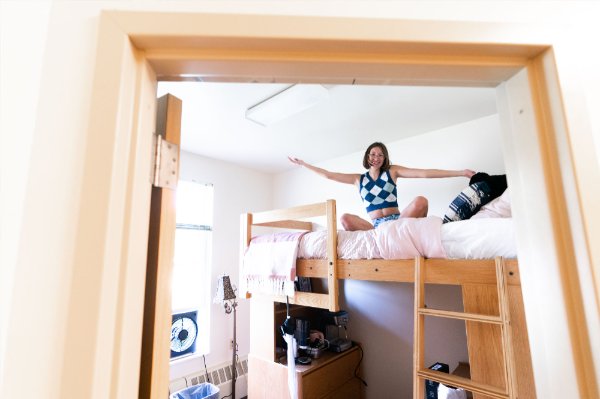 A person sits in their lofted bed in a dorm room.