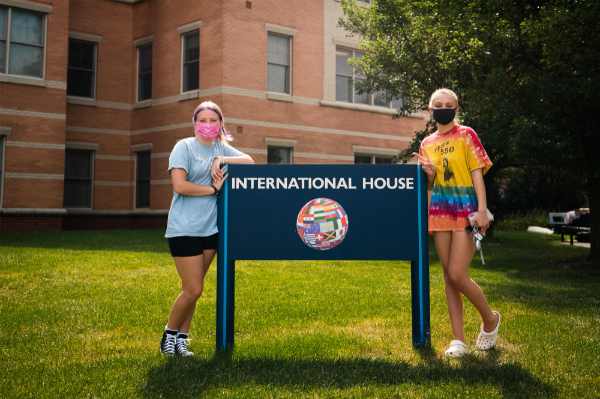 Two people in face coverings stand next to a sign that reads "International House"