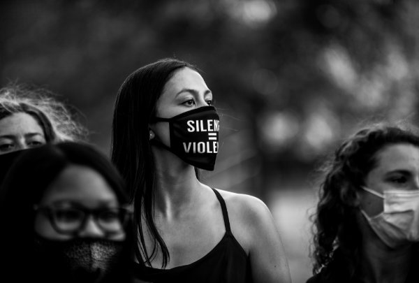 A black and white photo of a woman wearing a "silence is violence" face covering