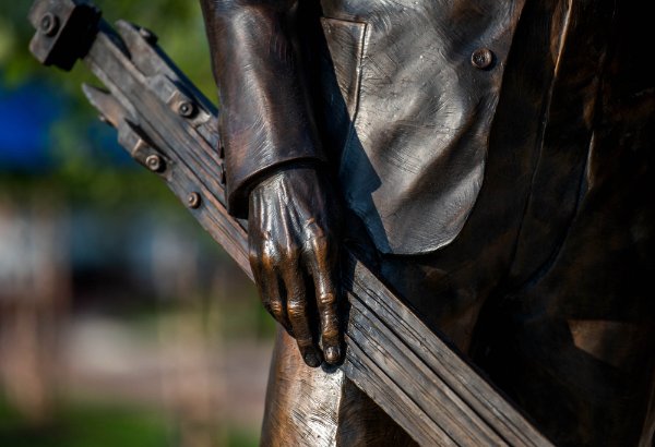 A detail image of a bronze sculpture shows a hand holding a piece of art equipment.