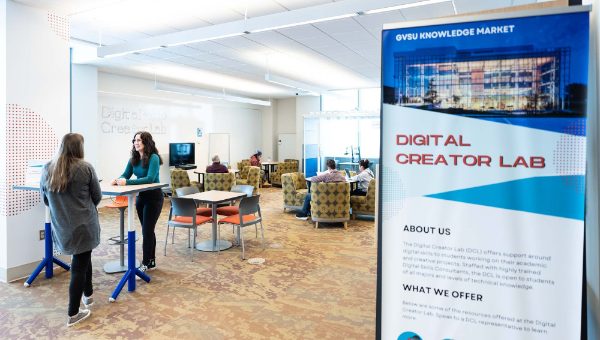 A photo of the Digital Creator Lab. Two students stand and talk, while others utilize other aspects of the space in the background. 