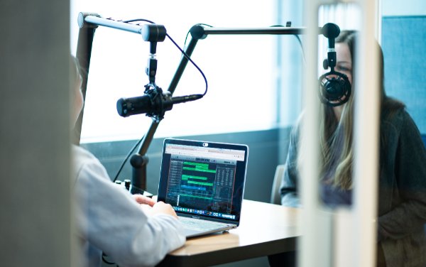 Two students sit in a podcast recording booth at the Digital Creator Lab.