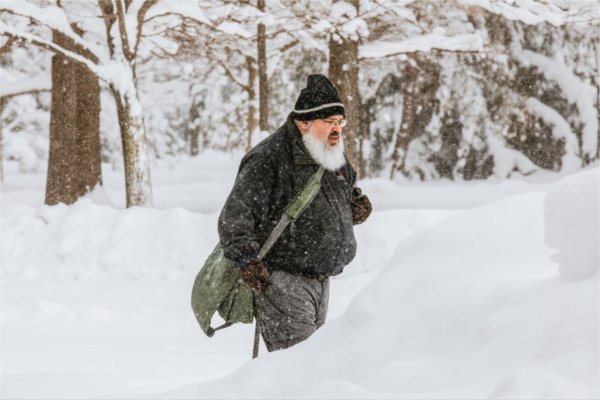  A person with a large white beard and winter hat makes their way through a wintry college campus. 