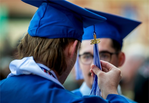Close-up of a person holding on to their graduation tassel from behind. The number 2023 also hangs on the tassel. 