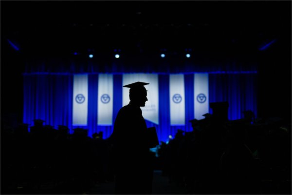 Silhouette of a person in a cap and gown against the background of the Commencement stage and decoration.