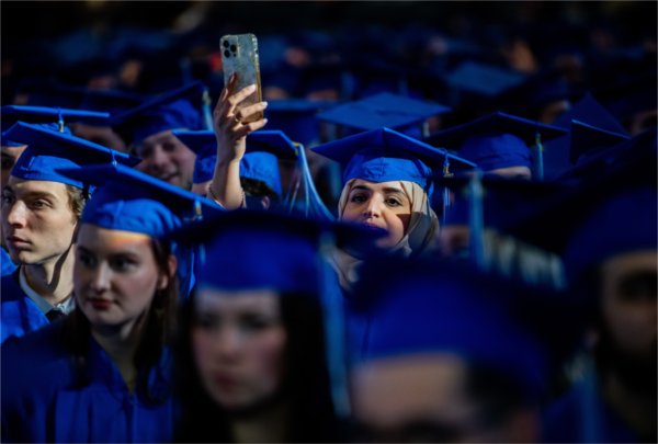 A graduate holds up a cell phone over all the other graduates' heads.
