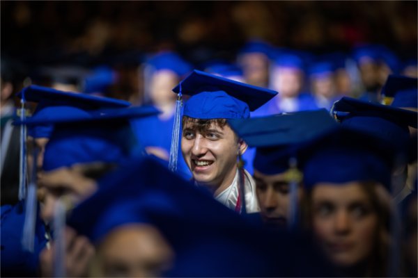 A person wearing a cap and gown smiles while surrounded in a sea of other soon-to-be graduates.