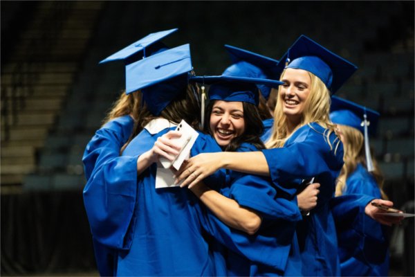 A smiling group of people in caps and gowns all hug each other.