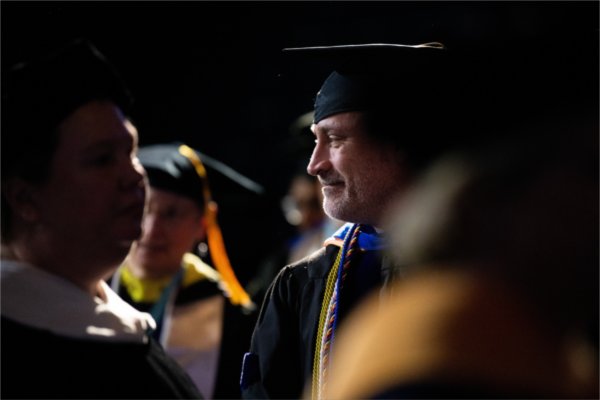A faculty member in academic regalia smiles while recessing after the ceremony. 