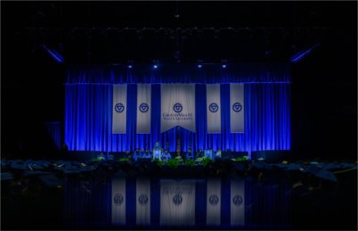 Wide photo of the stage at Commencement with a person speaking on stage.