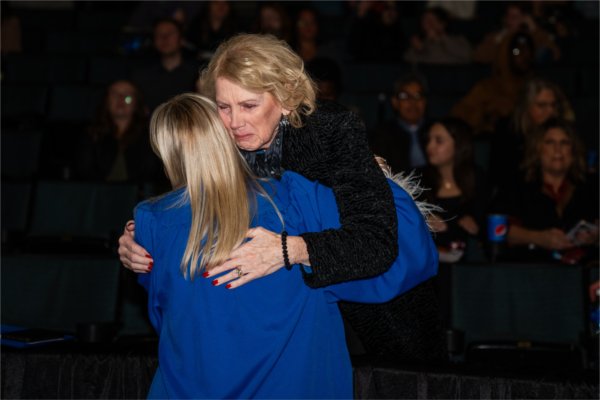A soon-to-be graduate in her gown, hugs her grandmother in the arena. 
