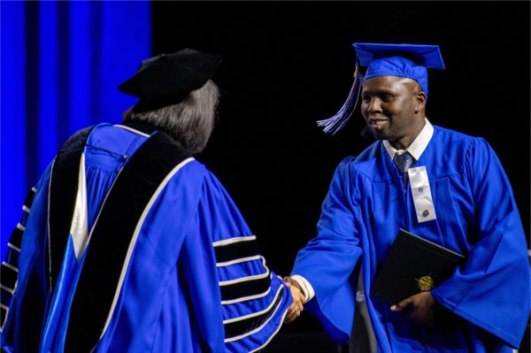 A person in cap and gown holding their diploma, shakes hands with a person dressed in academic regalia. 