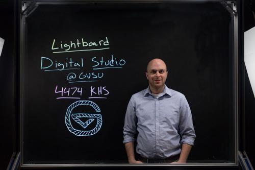 Photo by Christi Wiltenburg  Justin Melick, digital media developer, stands behind the lighboard in the Digital Studio in the Kindschi Hall of Science. Melick helps faculty members create videos using the lightboard.   