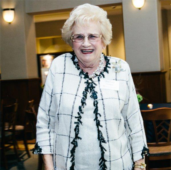 Barbara Gordon in white blazer with black trim, she is wearing glasses and has gray hair