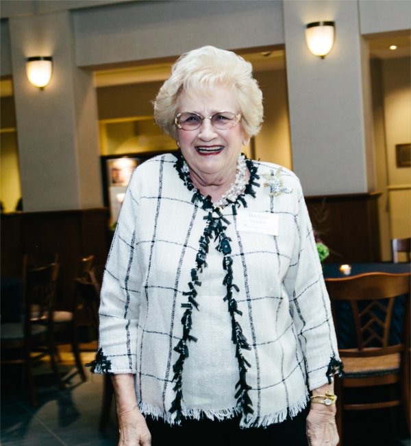 Barbara Gordon in white blazer with black trim, she has gray hair and is wearing glasses