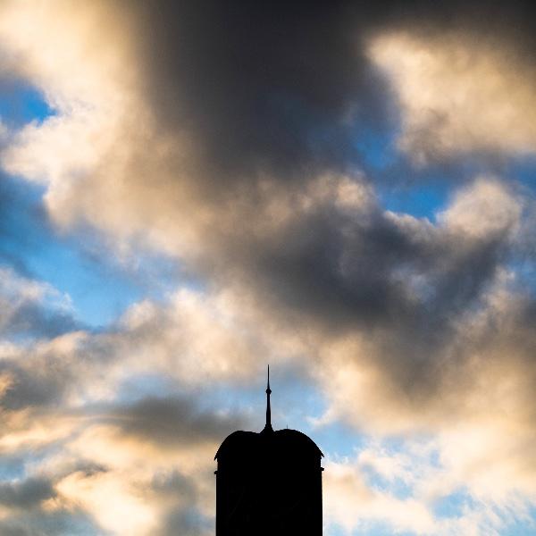 Silhouette of carillon tower against a blue sky with puffy clouds.