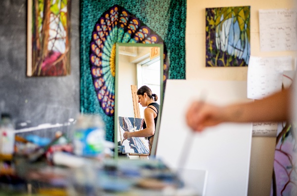 A college student is reflected in a mirror as she paints. 