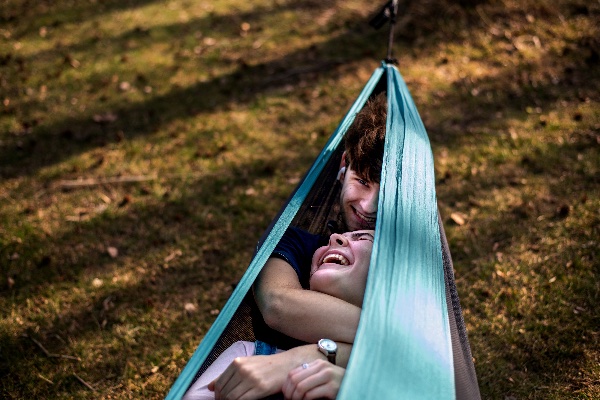 A couple snuggles in a teal hammock while laughing together.