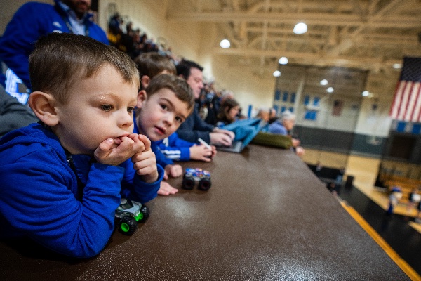  Two small children play with toy cars while watching an event in an arena. 