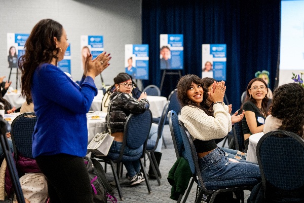  A room full of college students and participants clap and laugh together. 