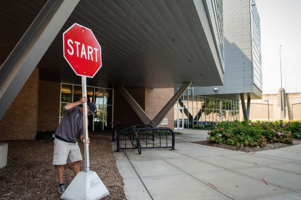 A person holds onto a pole containing the a red sign with the word "start" that was placed next to an outdoor walkway.