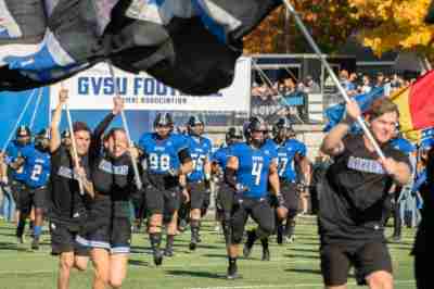 GVSU football team and cheerleaders running onto field at start of Homecoming game