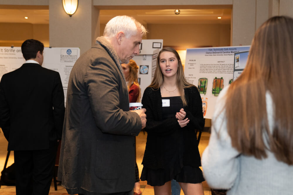 A photo of students presenting their research to those viewing their posters.