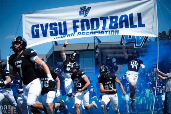 GVSU football players run underneath a banner reading, "GVSU Football." 