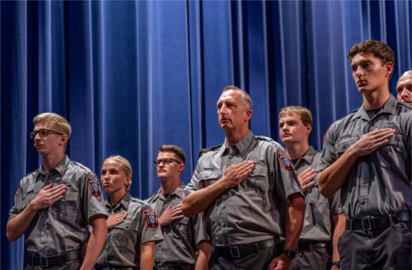 Police academy graduates stand in front of a blue curtain with their hands held over their hearts.