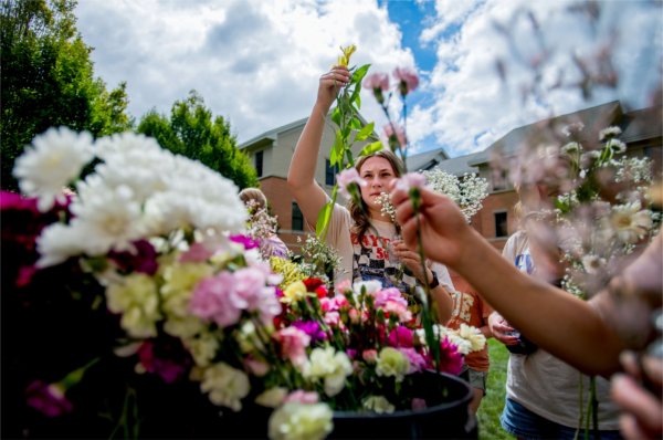 A student lifts a yellow flower from the buckets of flowers , with others reaching for flowers around her.