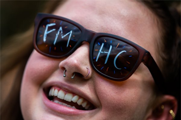 A close-up of a student smiling wearing sunglasses with the letters 'FMHC' drawn on the lenses.