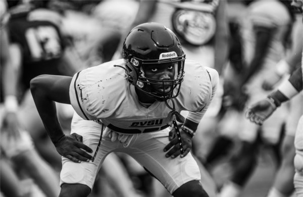 A black and white photo of a football player looking forward while stretching.