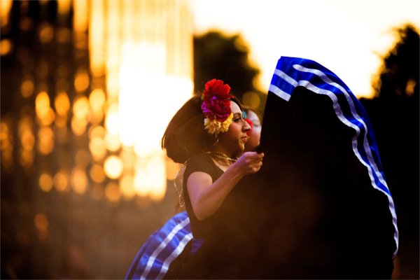 A person with colorful flowers in her hair dances while warm golden light shines behind her.
