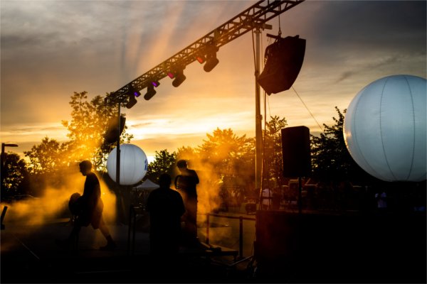 Stage crew members are silhouetted against golden sunlight as they set up equipment.