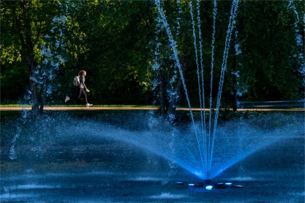 A close-up of a fountain with blue lights. A student wearing a backpack runs along the sidewalk in the background.