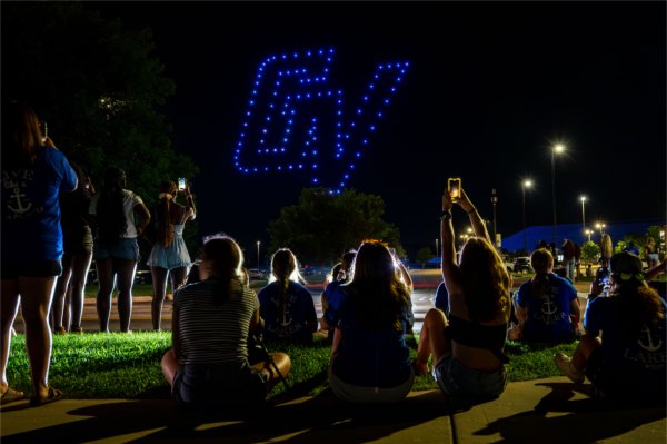 Students watch a drone show as the GV athletics logo is created in the sky with blue lights from the drones.
