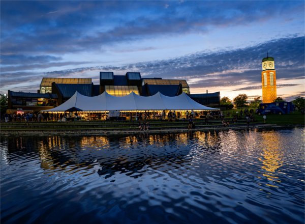 Students gather near amlarge white tent that sits by Zumberge pond while a Carillon Cook tower is illuminated in the background.