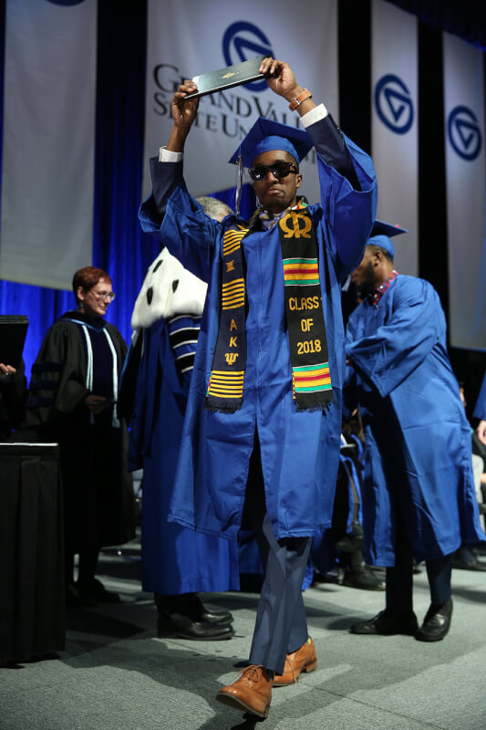 man walking across stage holding diploma