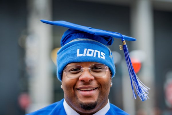 A graduate poses for a photo wearing a Detroit Lions beanie under his graduation cap.