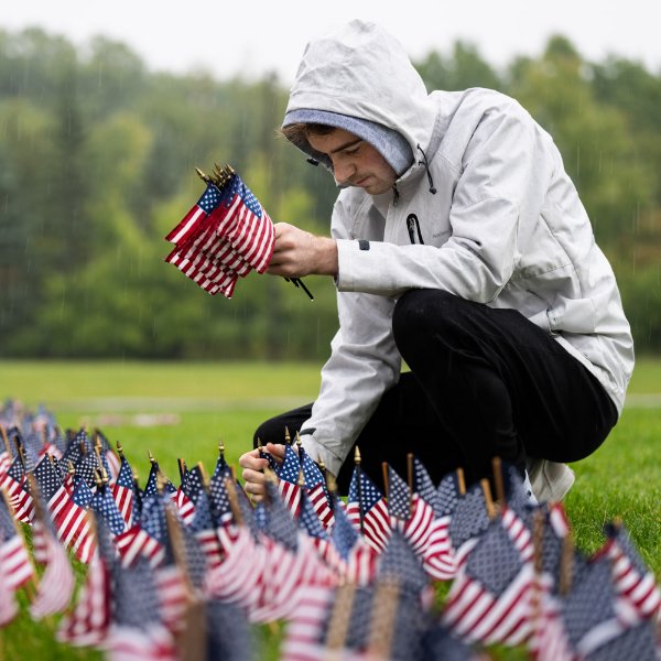 A person kneels while placing small American flags in the ground.