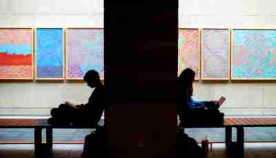 Two college students are silhouetted as they do school work in front of framed art. 