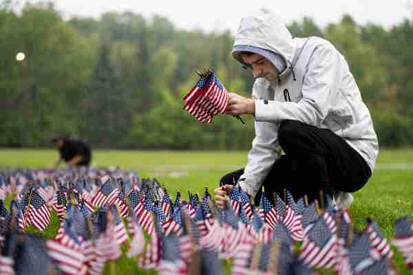 A college student places small American flags into the ground while it's raining.  