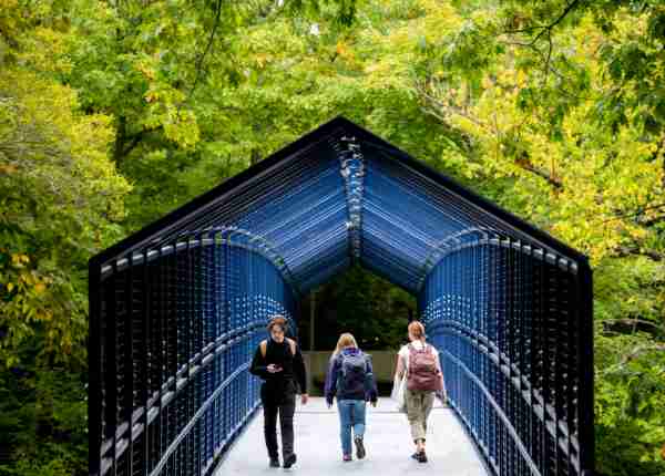 Students walk over a blue bridge among green trees.  