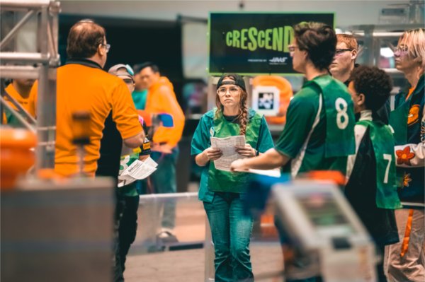 team members in green shirts consult with orange shirt coach at Robotics event