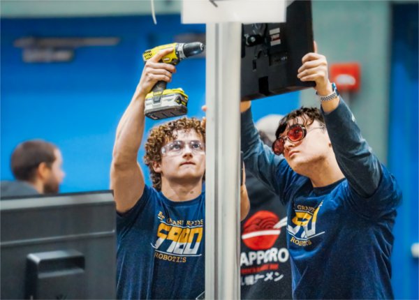 two team members from East Grand Rapids hold a drill and fix their robot