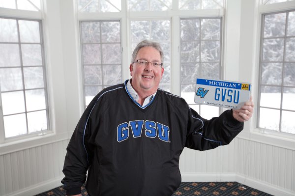 Bob Stoll holds a license plate with GVSU on it, a GVSU specialized plate