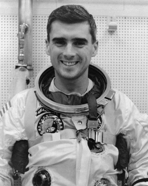 In a black and white photo, a person wearing a space suit smiles for the camera.